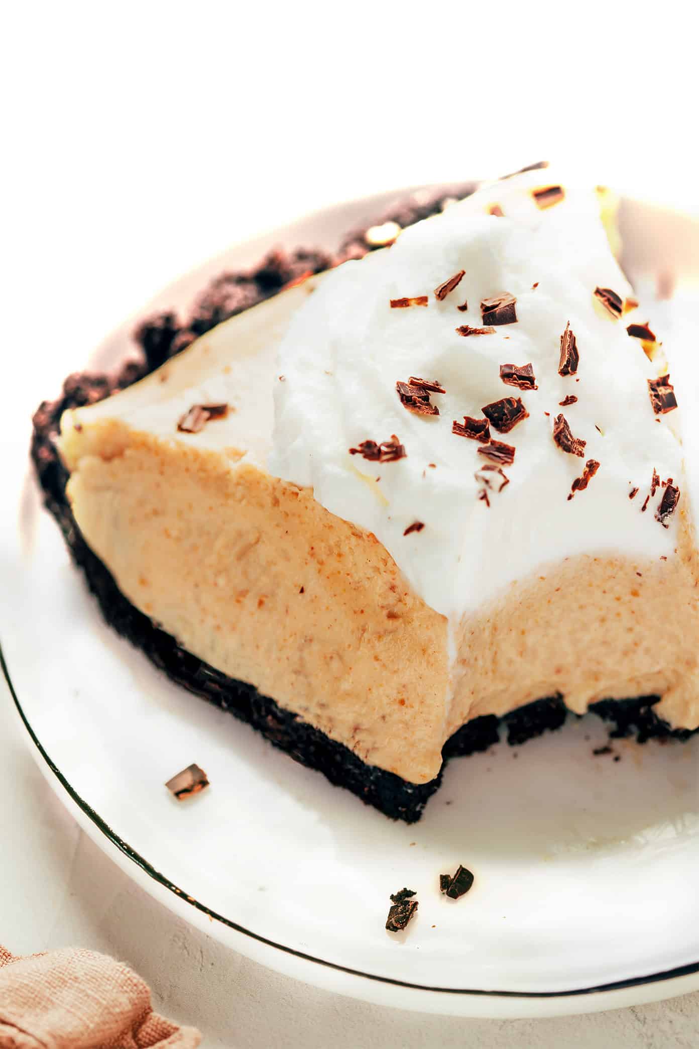 This classic no-bake peanut butter pie recipe features a chocolate Oreo crust and a fluffy peanut butter filling. The perfect easy summer dessert! | gimmesomeoven.com Slice of peanut butter pie with whipped cream